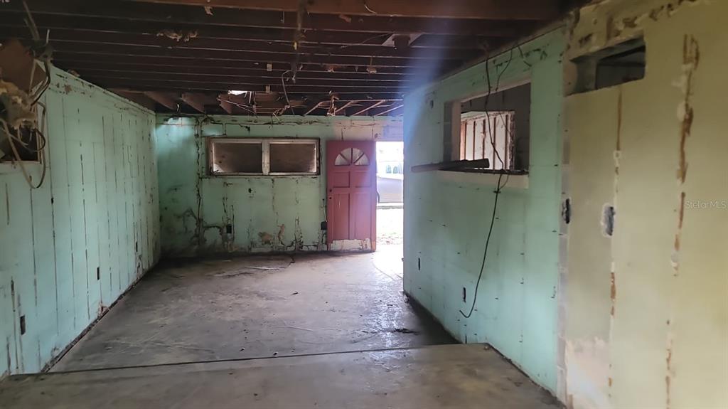 An unfinished room with exposed ceiling joists, light green walls, and a red exterior door — 1024 W FAIRBANKS AVENUE, ORLANDO, FL