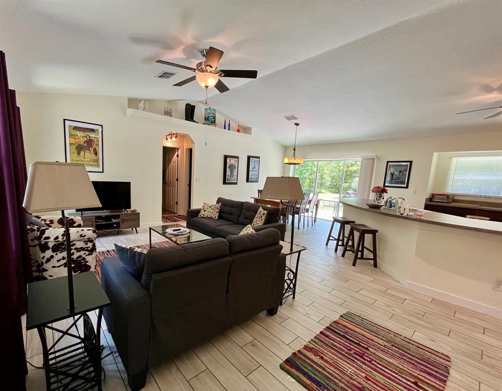 A living room with tile floors, a dark sofa, a ceiling fan, and a breakfast bar — 7710 NW 14TH STREET, OCALA, FL