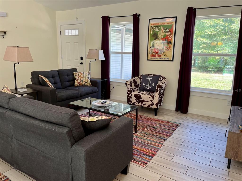 A living room features gray sofas, a patterned armchair, a glass coffee table, and colorful rug — 7710 NW 14TH STREET, OCALA, FL