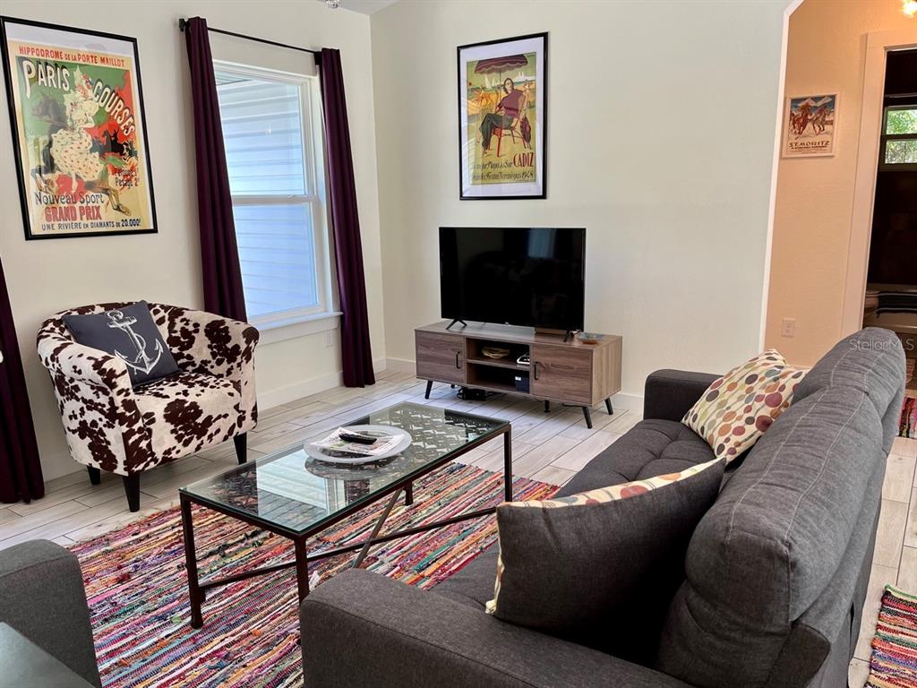 A living room features a grey sofa, a cow-print armchair, a glass coffee table, and television — 7710 NW 14TH STREET, OCALA, FL