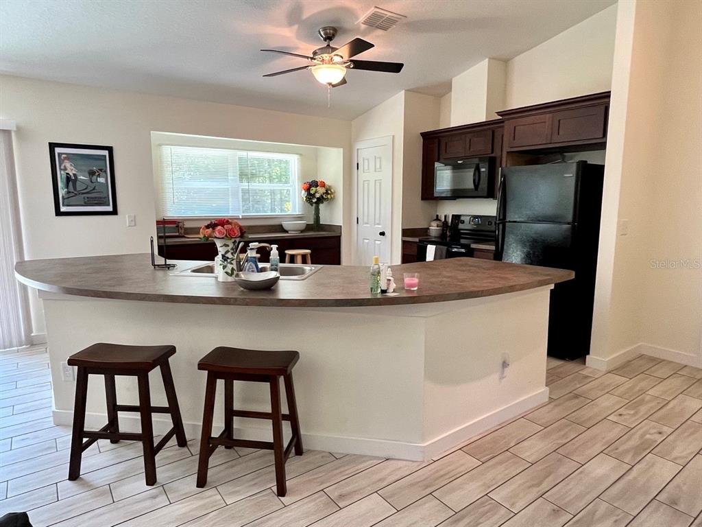 A kitchen features a curved breakfast bar, dark wood cabinets, black appliances, and light tile flooring — 7710 NW 14TH STREET, OCALA, FL