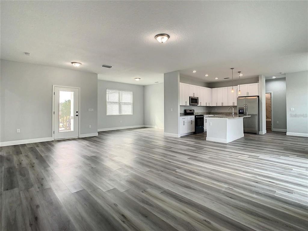 An open-concept living area features light gray walls, wood-look flooring, and a white kitchen — 15504 GREENWOOD AVENUE, PORT CHARLOTTE, FL
