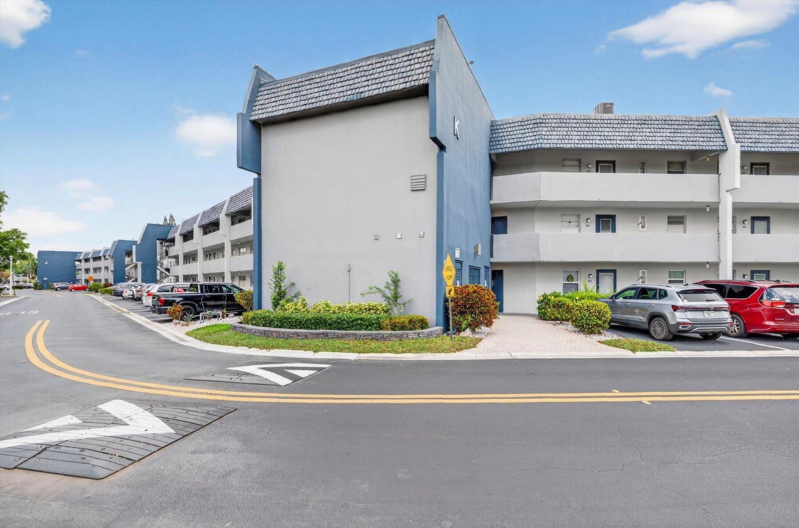A three-story apartment building with a gray facade and blue trim stands near a road — 7787 Golf Circle Drive # k, Margate FL 33063, MARGATE, FL