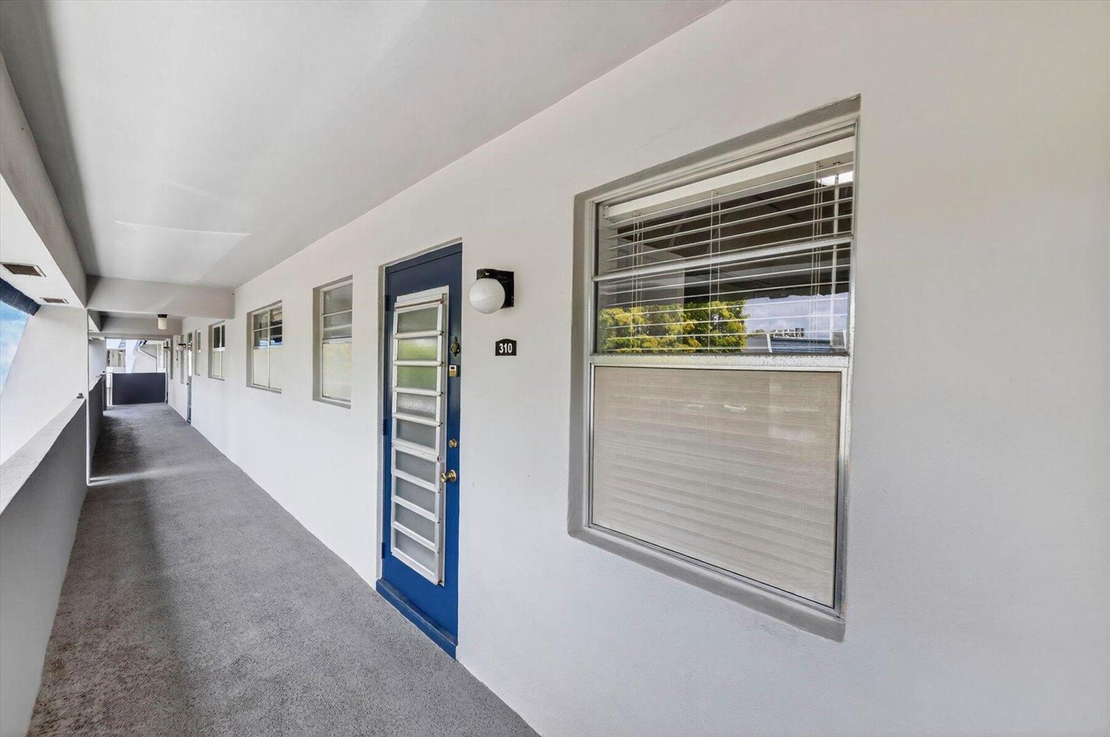 An exterior view of a building hallway with a blue door numbered 310 — 7787 Golf Circle Drive # k, Margate FL 33063, MARGATE, FL