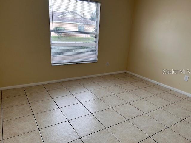 An empty room features beige walls, light-colored square floor tiles, and a window with blinds — 40 E COUNTRY COVE WAY, KISSIMMEE, FL