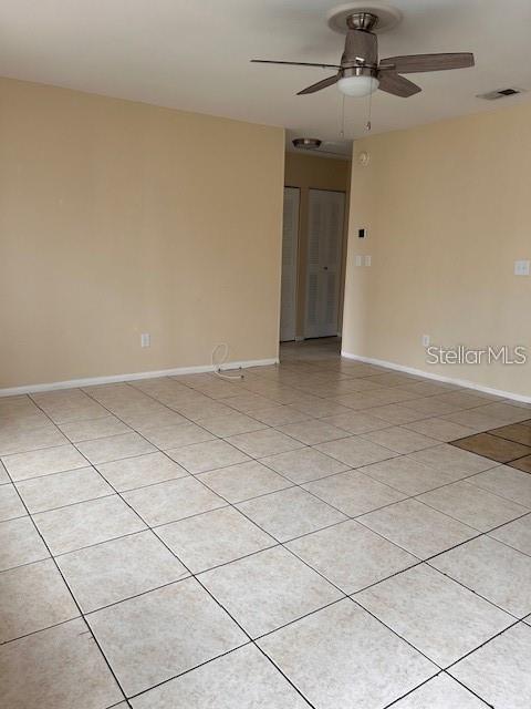 An empty room features light-colored tile flooring, beige walls, and a ceiling fan — 40 E COUNTRY COVE WAY, KISSIMMEE, FL