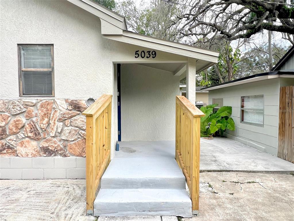 The exterior of a house features a concrete porch with wooden railings and stone siding — 5045 GREEN KEY ROAD, NEW PORT RICHEY, FL