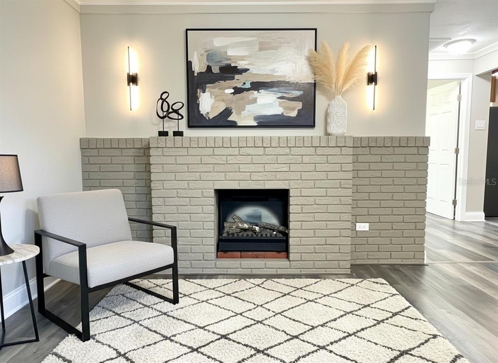 A living room features a light gray brick fireplace, a modern armchair, and wall sconces — 5045 GREEN KEY ROAD, NEW PORT RICHEY, FL