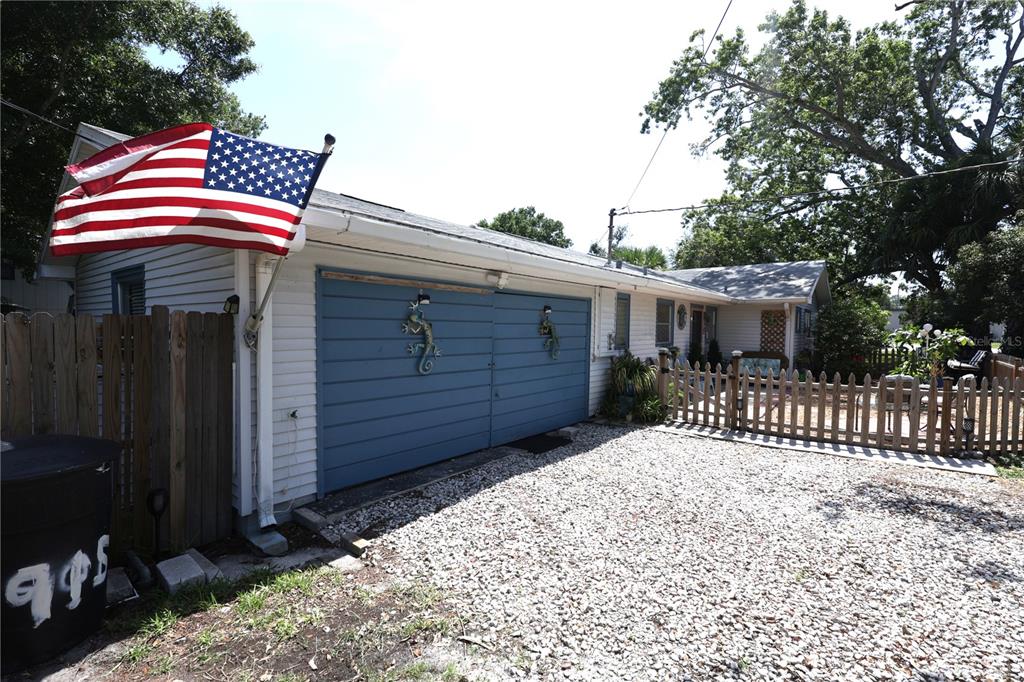 A gravel driveway leads to a house with blue garage doors and an American flag — 915 DEMPSEY STREET, CLEARWATER, FL