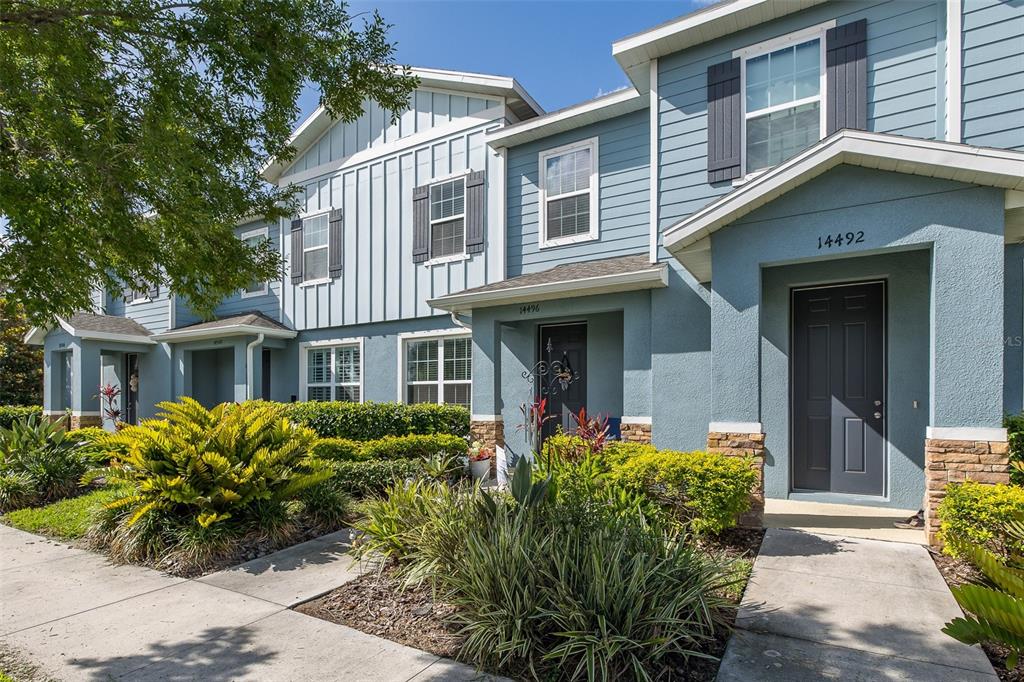 A row of blue two-story townhomes with stone accents and landscaped front yards — 14496 PROMENADE PARKWAY, ODESSA, FL