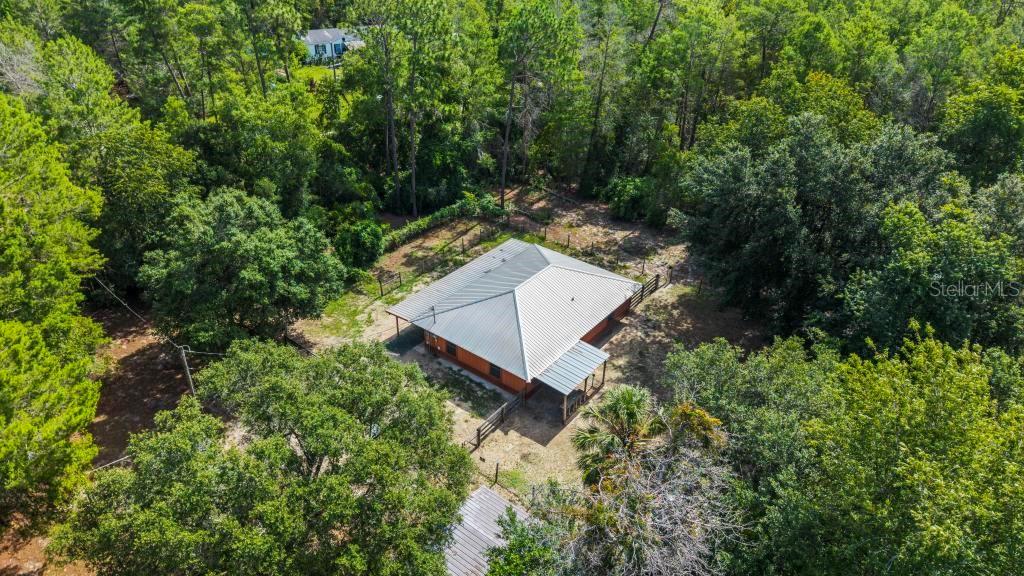 An aerial view shows a house with a metal roof surrounded by dense trees — 24607 POLAR BEAR ROAD, PAISLEY, FL