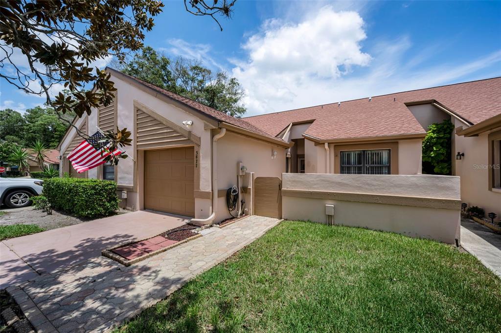 A tan single-story house features a garage, a paved walkway, and a small front lawn — 3477 HILLMOOR DRIVE, PALM HARBOR, FL