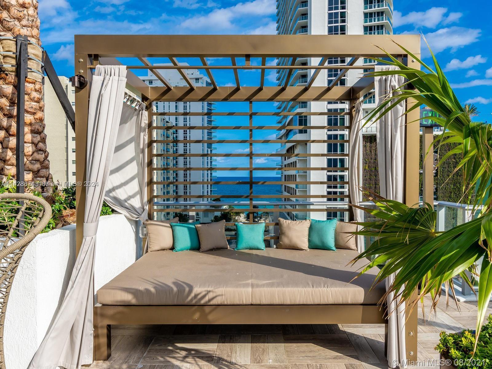 A poolside cabana with a daybed and curtains overlooks the ocean and high-rise buildings — 4010 S Ocean Dr # R301, Hollywood FL 33019, HOLLYWOOD, FL
