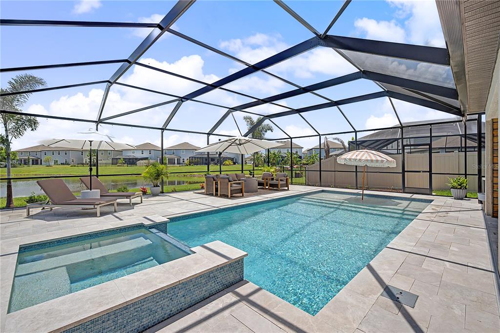 A screened-in pool and spa area with patio furniture overlooking a pond and houses — 7747 ABBY BROOKS CIRCLE, WESLEY CHAPEL, FL