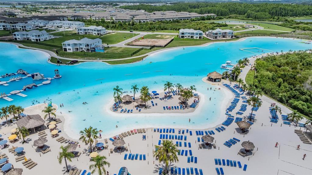 An aerial view shows a large turquoise lagoon with a central island and sandy beach — 7747 ABBY BROOKS CIRCLE, WESLEY CHAPEL, FL
