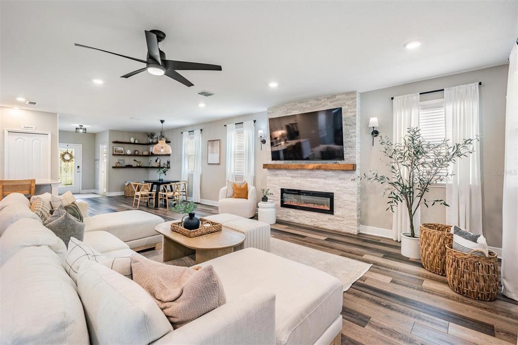 A living room features a stone fireplace, a large sectional sofa, and wood-look flooring — 7747 ABBY BROOKS CIRCLE, WESLEY CHAPEL, FL