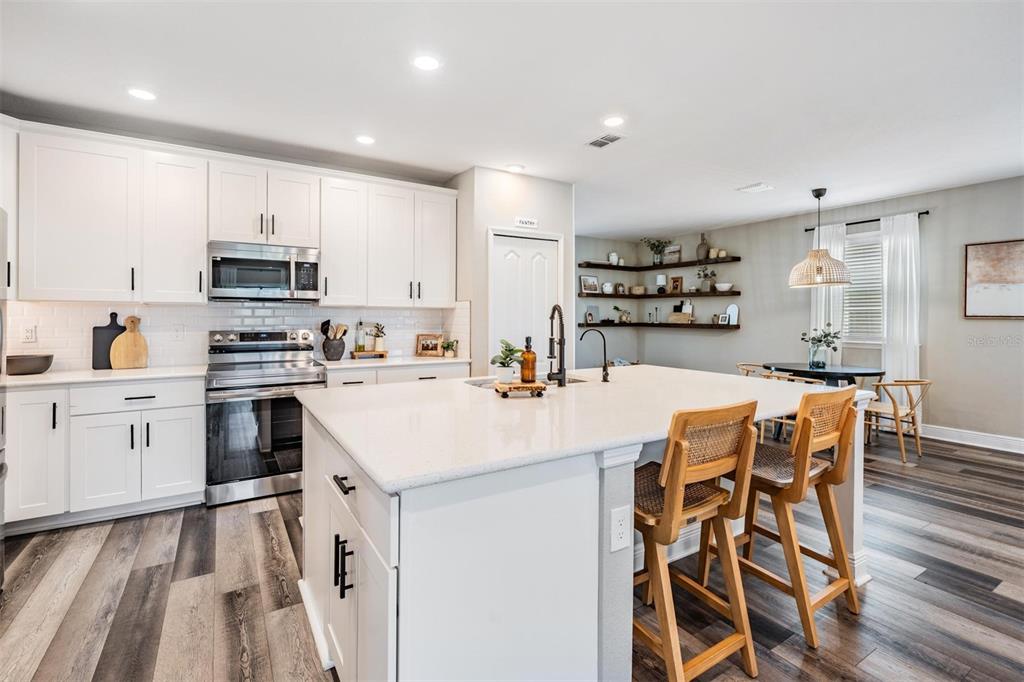 A modern kitchen features white cabinetry, a large quartz island, and wood-look plank flooring — 7747 ABBY BROOKS CIRCLE, WESLEY CHAPEL, FL
