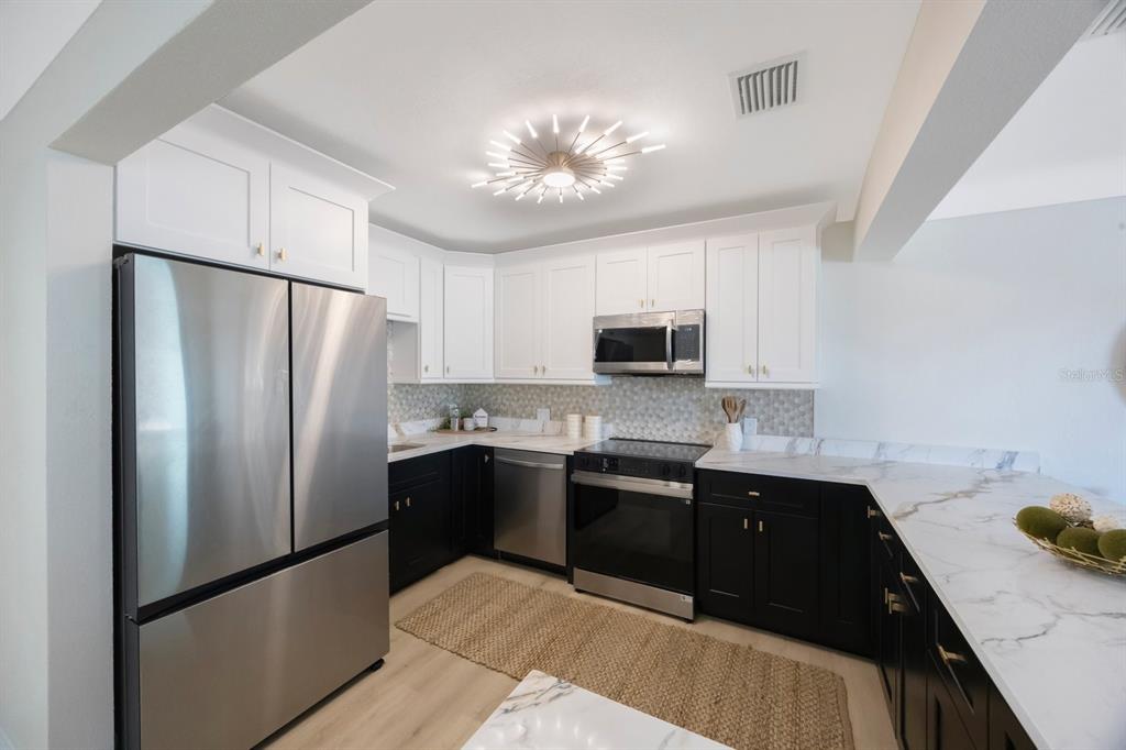 A kitchen features white upper cabinets, black lower cabinets, stainless steel appliances, and marble countertops — 280 41ST AVENUE, ST PETE BEACH, FL