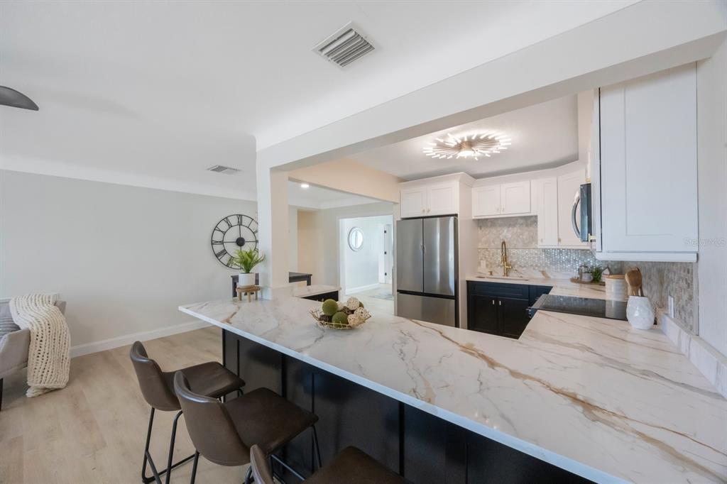 A kitchen with a marble-topped breakfast bar, stainless steel appliances, and dark lower cabinets — 280 41ST AVENUE, ST PETE BEACH, FL