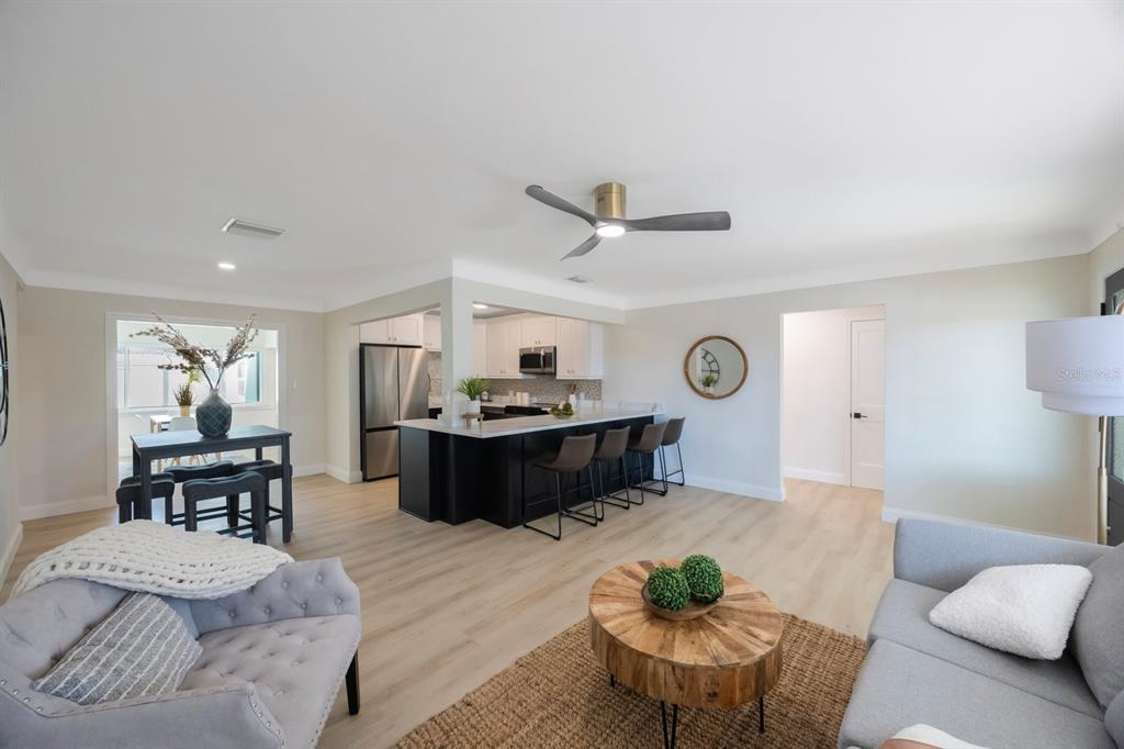An open-concept living room and kitchen featuring light wood floors and a dark kitchen island — 280 41ST AVENUE, ST PETE BEACH, FL
