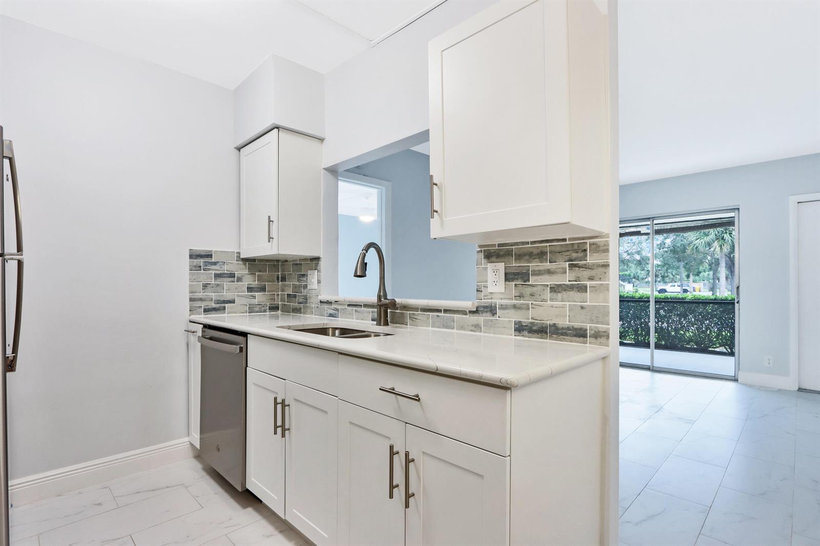 A kitchen features white cabinets, a quartz countertop, a stainless dishwasher, and a tiled backsplash — 6313 Chasewood Drive # B, Jupiter FL 33458, JUPITER, FL