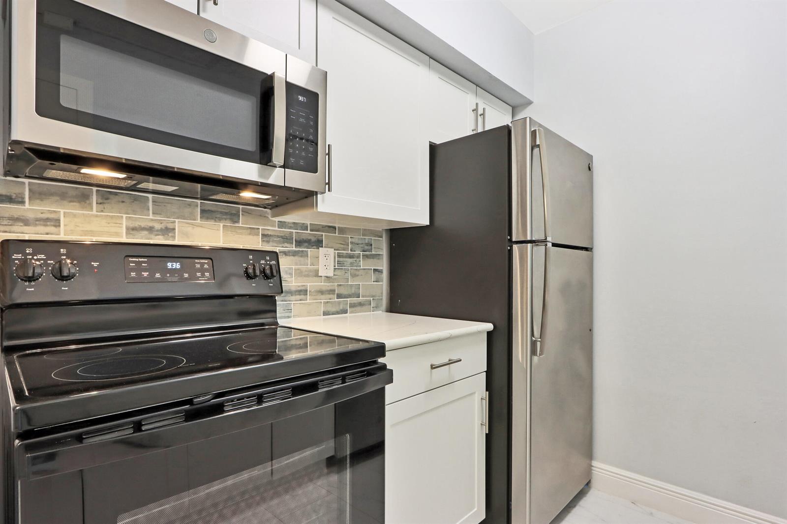 A kitchen features stainless steel appliances, white cabinets, and a blue-toned tiled backsplash — 6313 Chasewood Drive # B, Jupiter FL 33458, JUPITER, FL