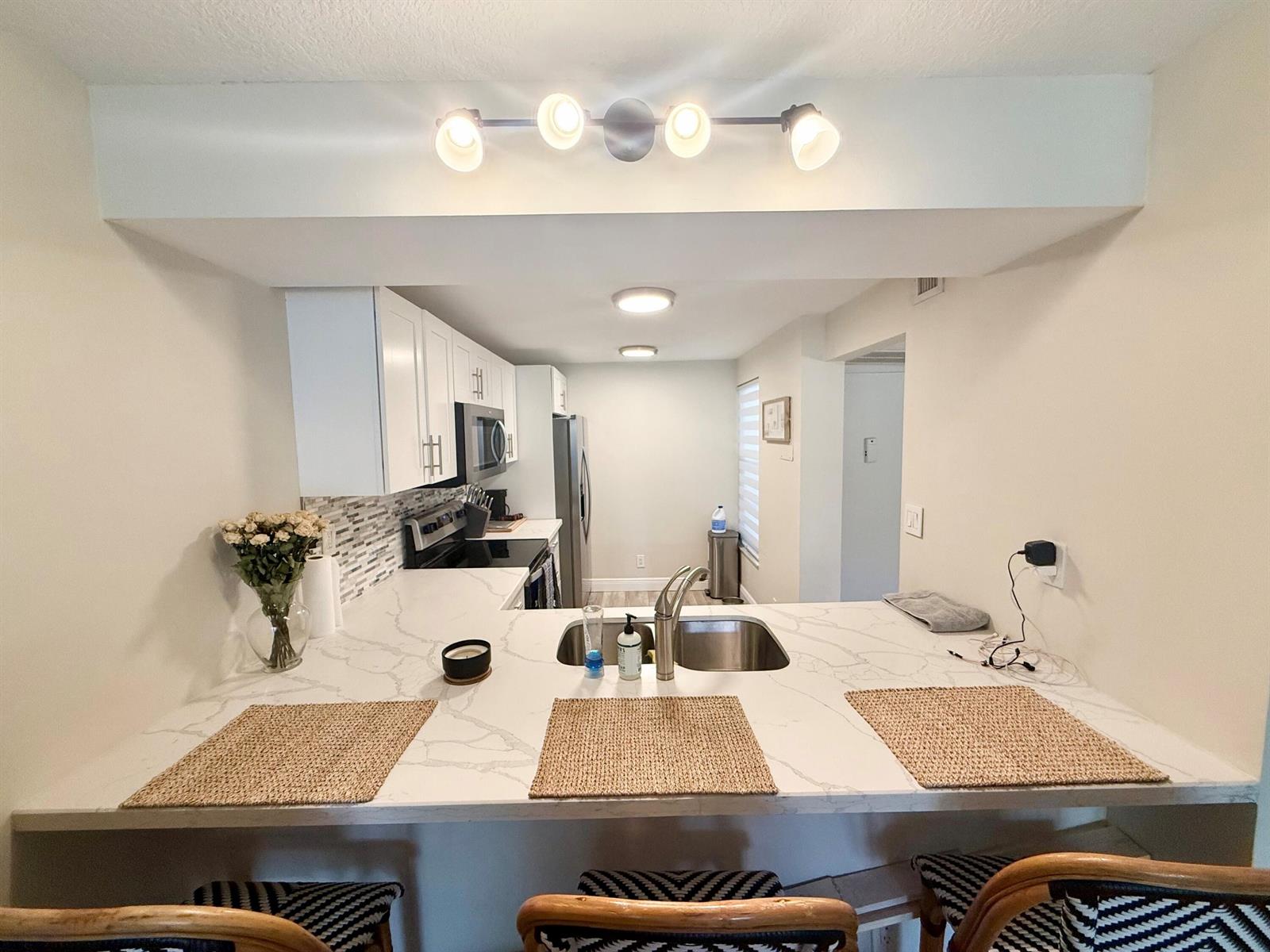 A kitchen with white cabinets, a quartz countertop, and a breakfast bar with three stools — 11 Royal Palm Way # 303, Boca Raton FL 33432, BOCA RATON, FL