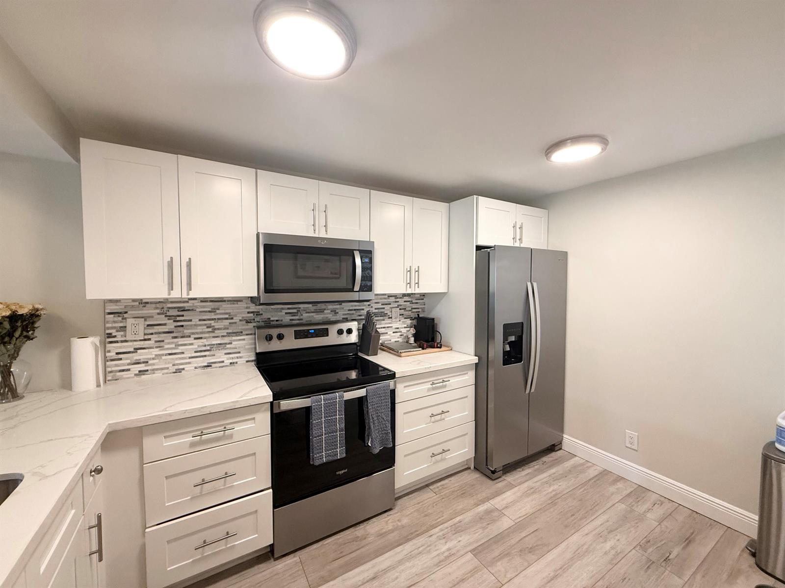 A kitchen features white cabinets, stainless steel appliances, a tiled backsplash, and light wood flooring — 11 Royal Palm Way # 303, Boca Raton FL 33432, BOCA RATON, FL