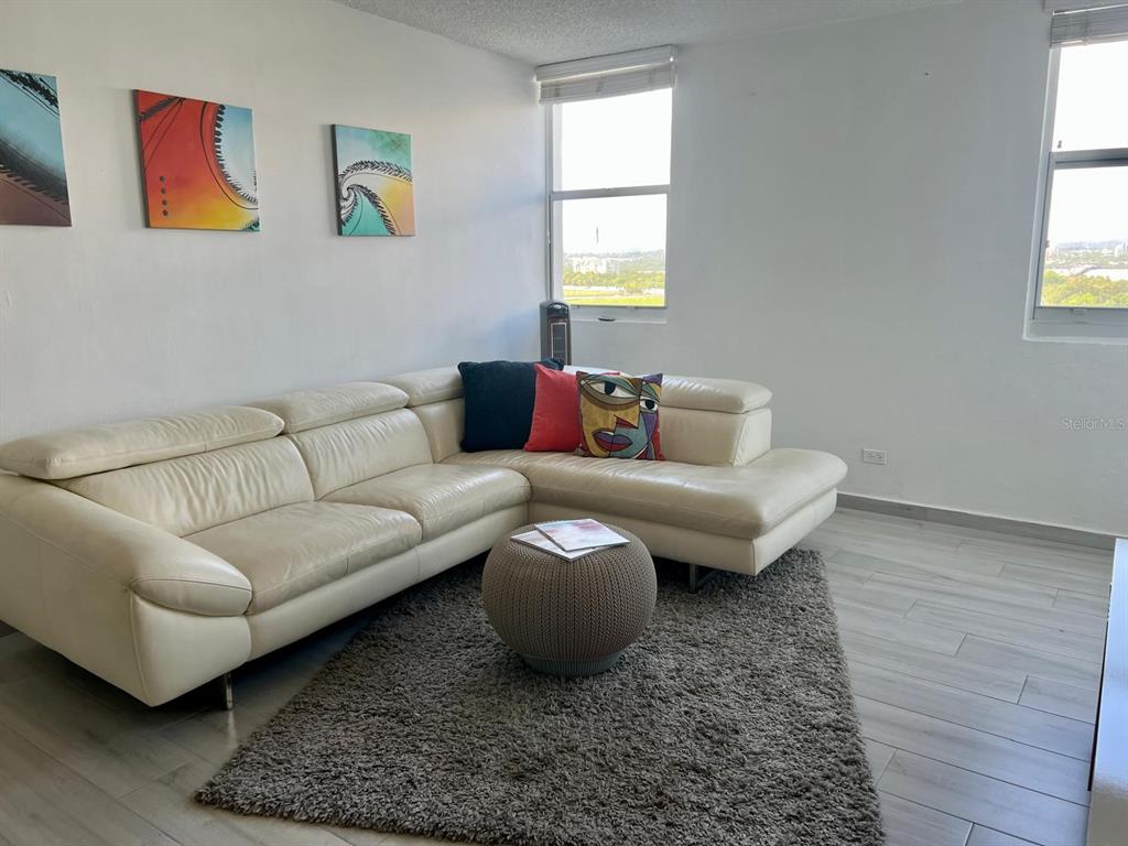 A living room features a white sectional sofa, a gray rug, and three wall-mounted paintings — 5890 JOSÉ M. TARTAK AVENUE UNIT 1104 A, CAROLINA, PR