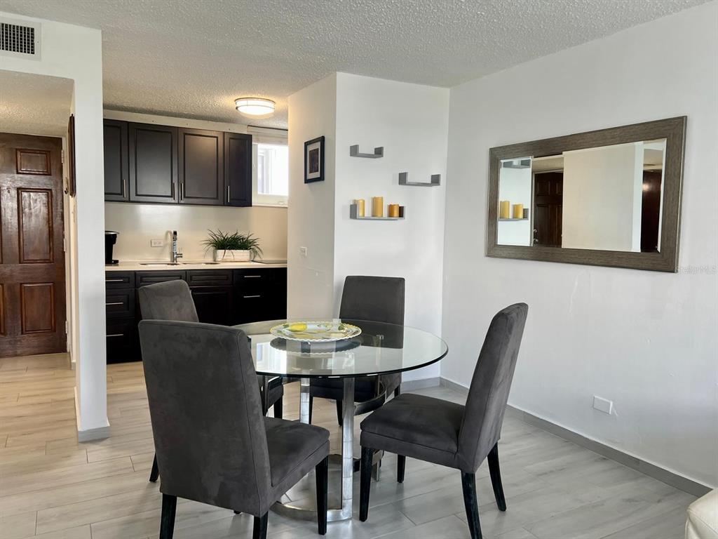 A dining area with a glass table and four gray chairs next to a kitchen — 5890 JOSÉ M. TARTAK AVENUE UNIT 1104 A, CAROLINA, PR