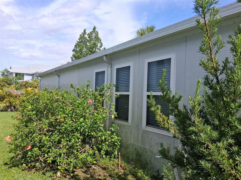 The exterior of a light-colored home features white-framed windows and surrounding landscaping — 24437 HARBORVIEW ROAD UNIT 36, PUNTA GORDA, FL