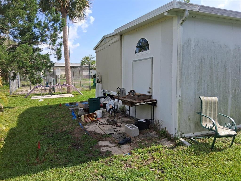 An exterior view of a mobile home side wall with a door, workbench, and chair — 24437 HARBORVIEW ROAD UNIT 36, PUNTA GORDA, FL