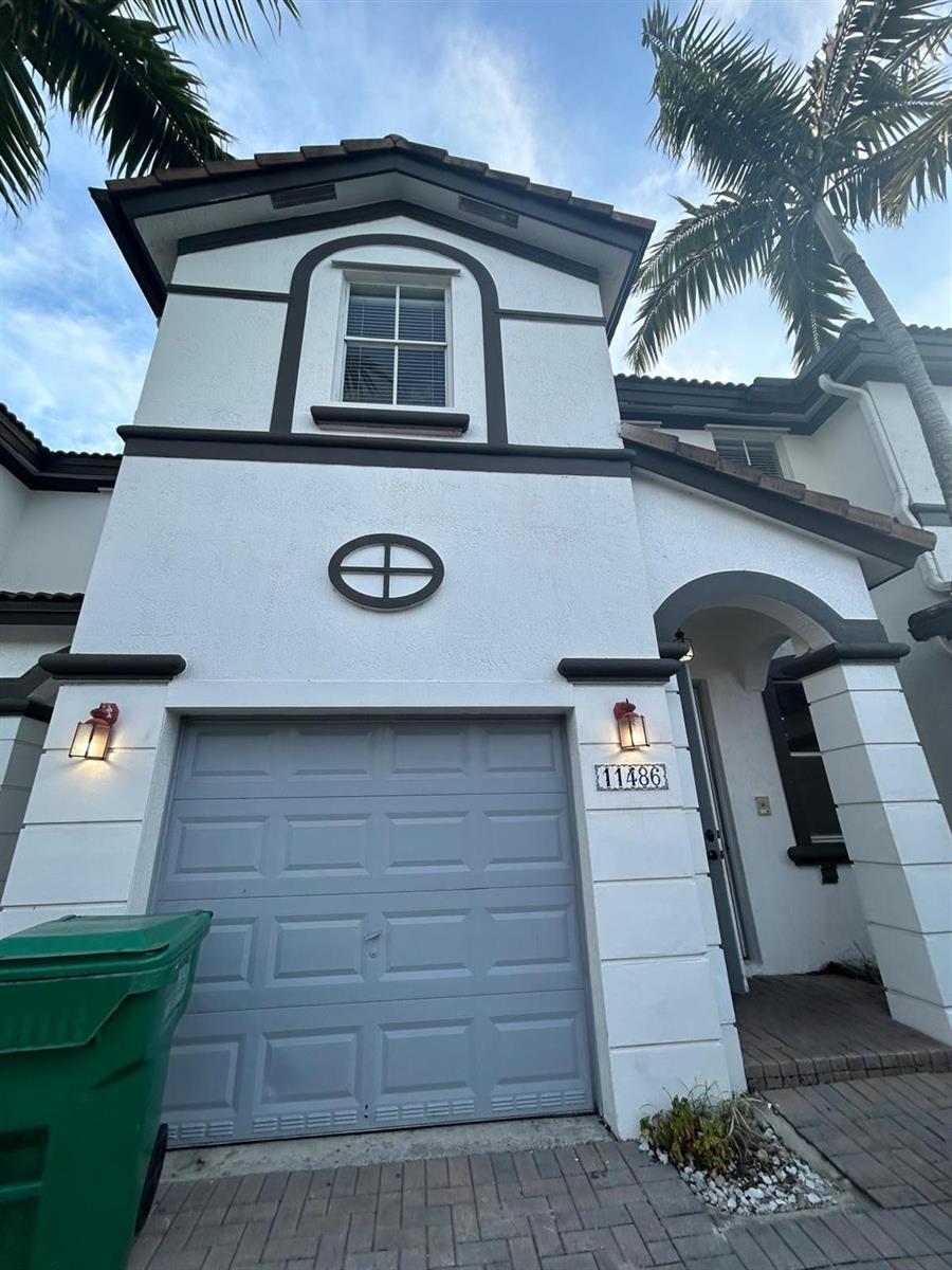 A two-story residential exterior features a light gray garage door, white stucco walls, and a palm tree — 11486 NW 77th Street, Doral FL 33178, DORAL, FL