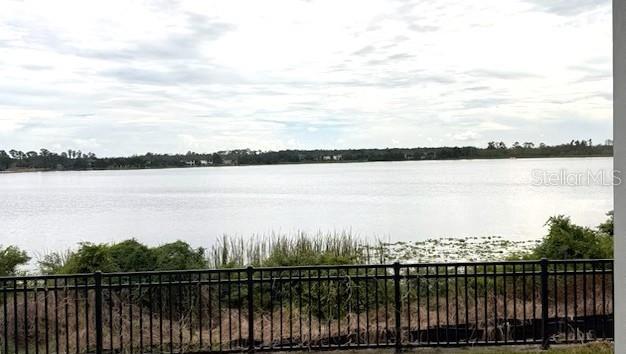 A view of a lake from a patio with a black metal fence in the foreground — 14168 LARKSPUR LAKE DRIVE, WINTER GARDEN, FL