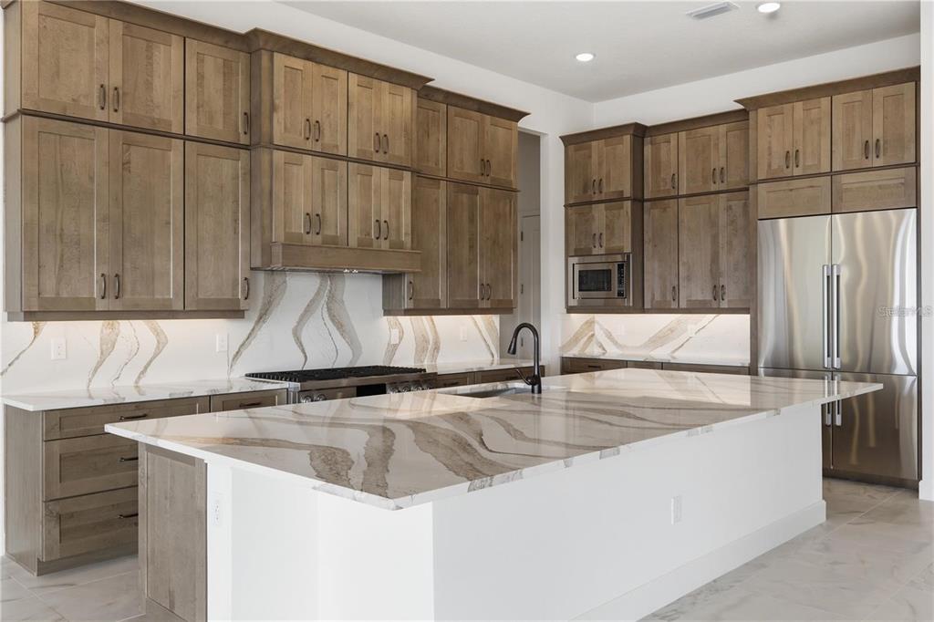 A modern kitchen features wood cabinets, a large white island, and marble-patterned countertops and backsplash — 14168 LARKSPUR LAKE DRIVE, WINTER GARDEN, FL