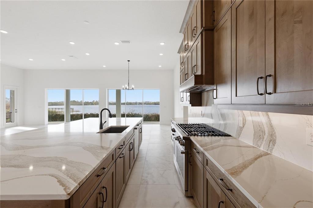 A modern kitchen features wood cabinets, white marble-patterned countertops, and large windows overlooking a lake — 14168 LARKSPUR LAKE DRIVE, WINTER GARDEN, FL