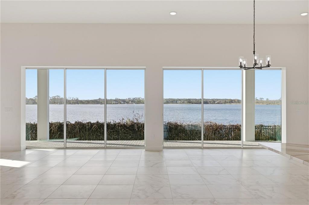 A bright, tiled room features large sliding glass doors overlooking a lake and distant shoreline — 14168 LARKSPUR LAKE DRIVE, WINTER GARDEN, FL