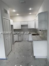 A kitchen features white cabinets, light-colored countertops, and white marble-patterned tile flooring — 1717 NW 70th St, Miami FL 33147, MIAMI, FL