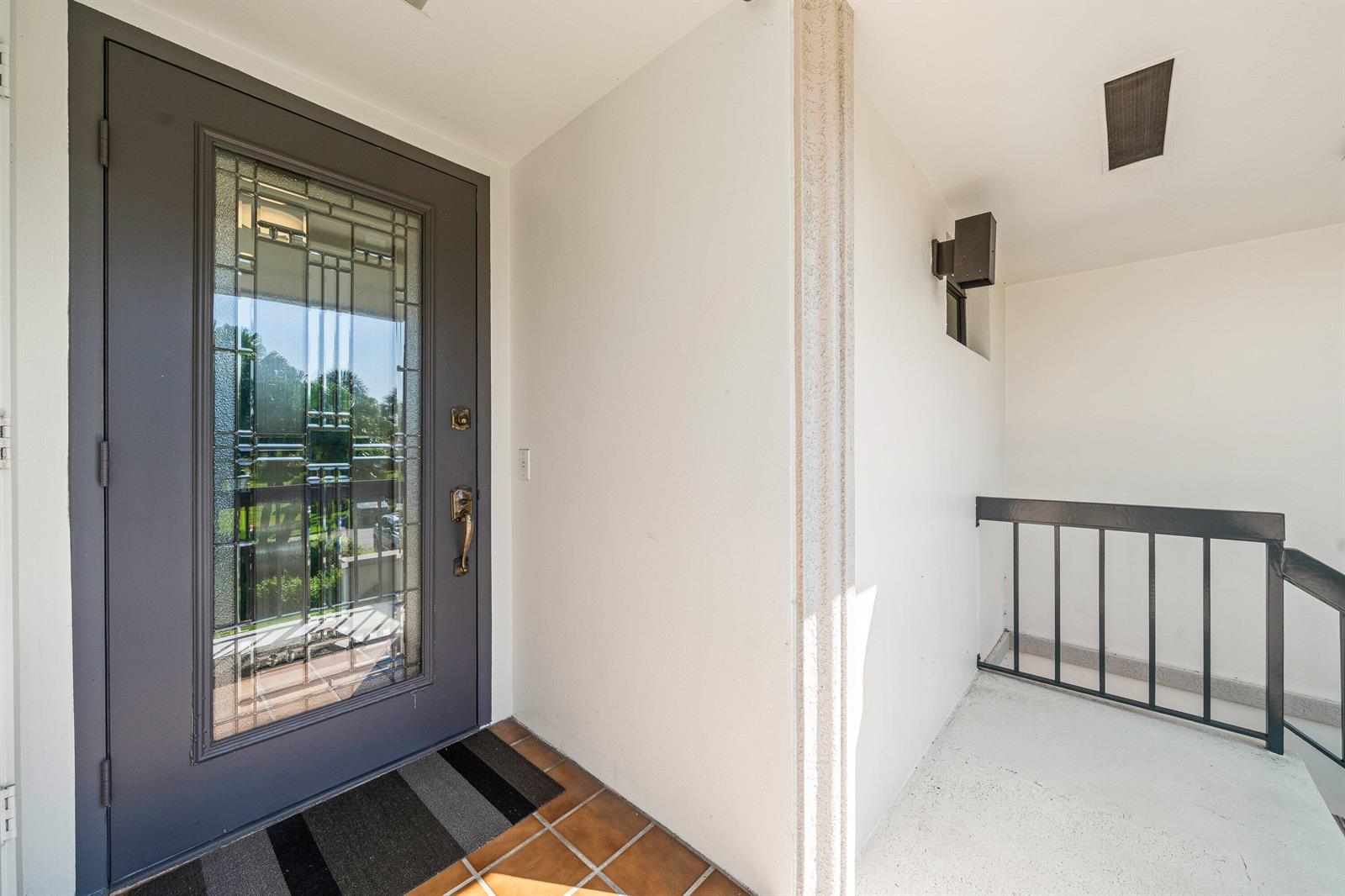 A gray front door with a decorative glass insert opens onto a tiled entryway porch — 10221 Quail Covey Road, Boynton Beach FL 33436, BOYNTON BEACH, FL