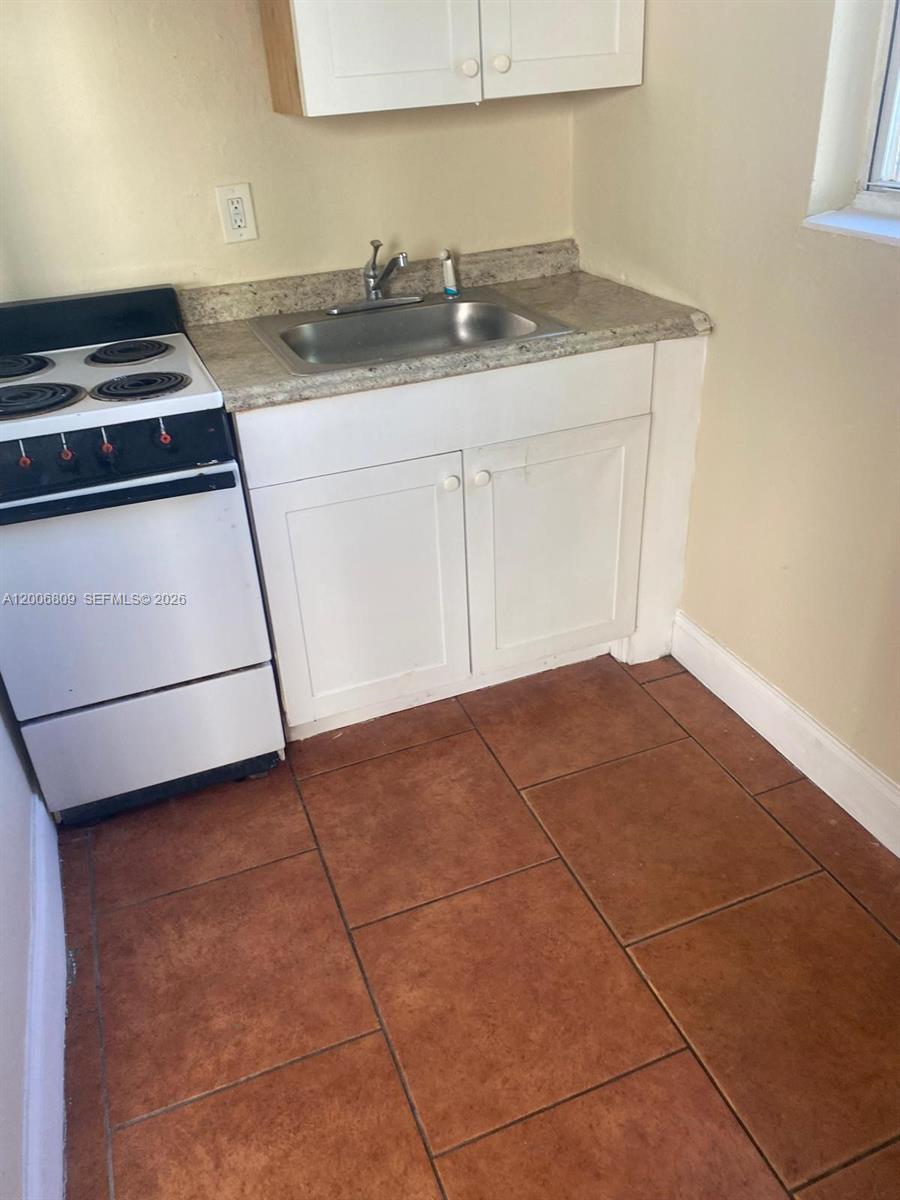 A small kitchen features a white stove, a stainless steel sink, and brown tile flooring — 1319 NW 60th St # 4, Miami FL 33142, MIAMI, FL