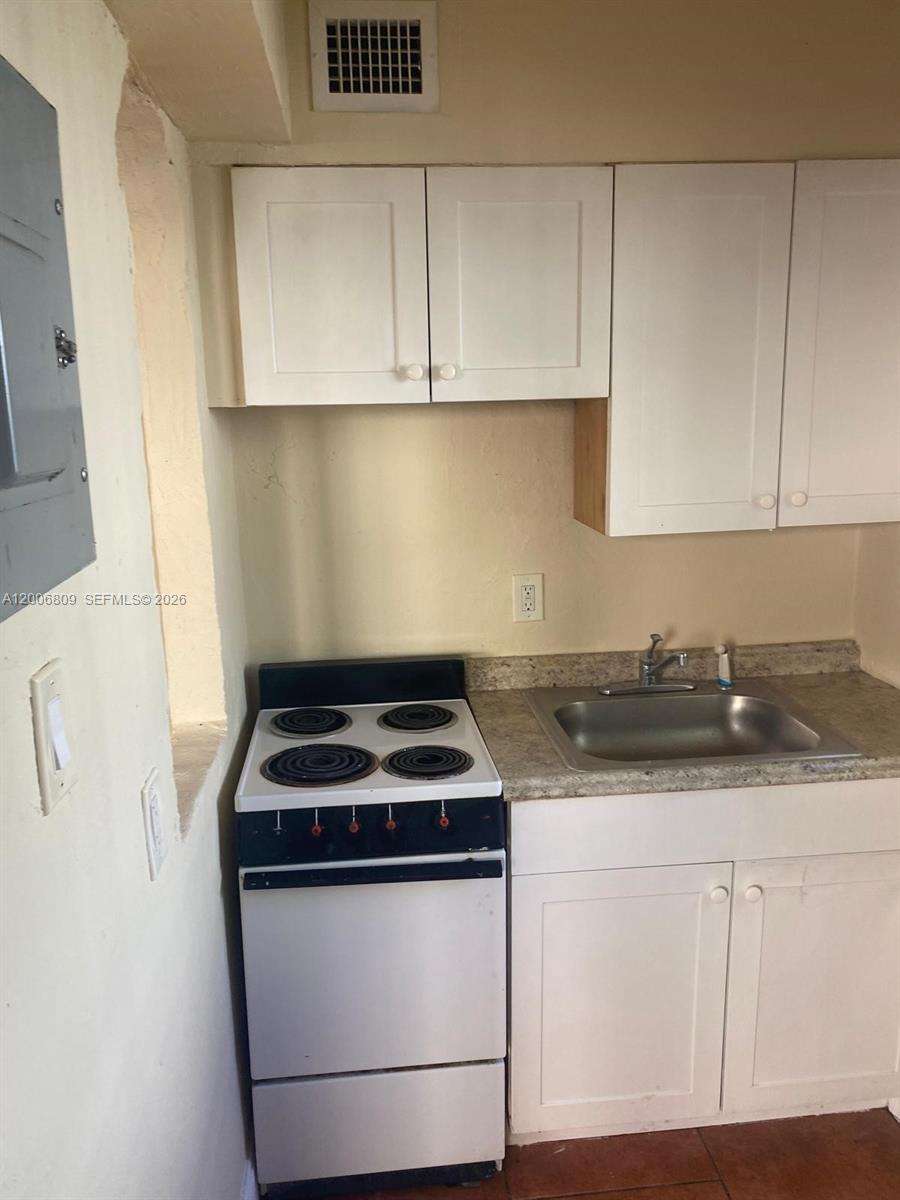 A small kitchen features white cabinets, a stainless steel sink, and a white electric stove — 1319 NW 60th St # 4, Miami FL 33142, MIAMI, FL