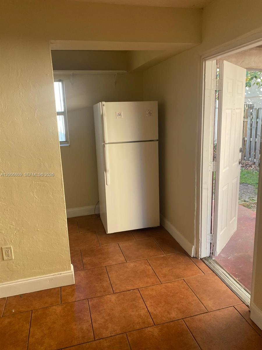 A white refrigerator stands in a tiled kitchen area next to an open exterior door — 1319 NW 60th St # 4, Miami FL 33142, MIAMI, FL