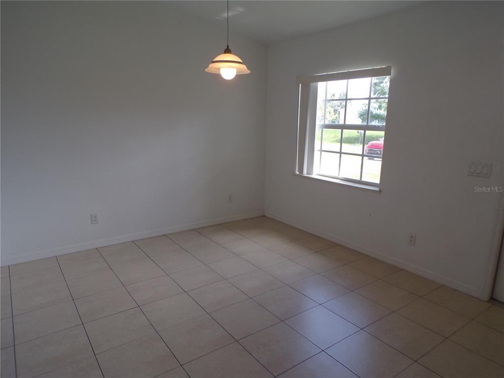 An empty room features white walls, beige tile flooring, a pendant light, and a window — 385 SUNFLOWER STREET UNIT A, PUNTA GORDA, FL