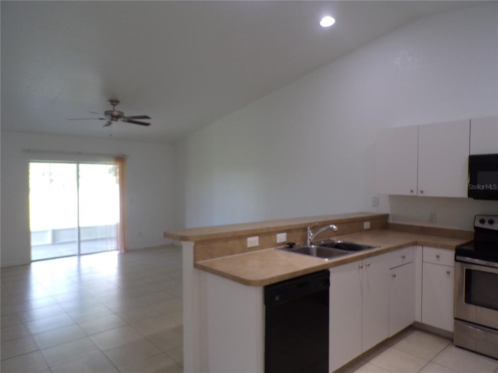 A kitchen with white cabinets and a breakfast bar overlooks an open living area — 385 SUNFLOWER STREET UNIT A, PUNTA GORDA, FL