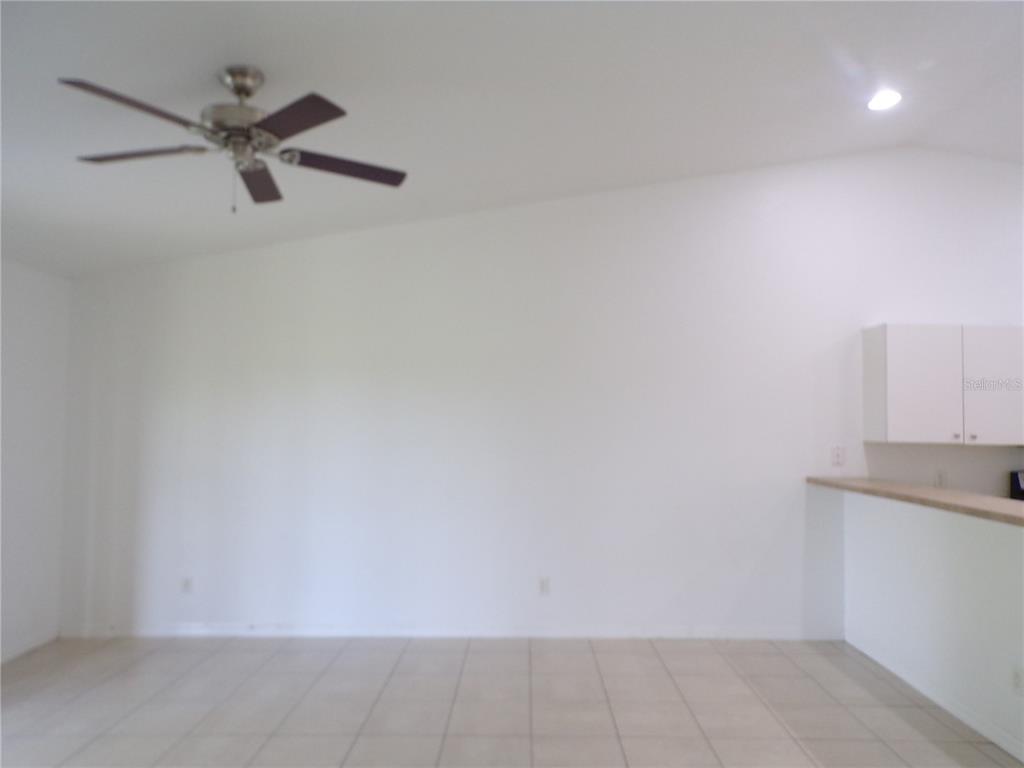 A bright, empty room features a ceiling fan, white walls, and light-colored tile flooring — 385 SUNFLOWER STREET UNIT A, PUNTA GORDA, FL