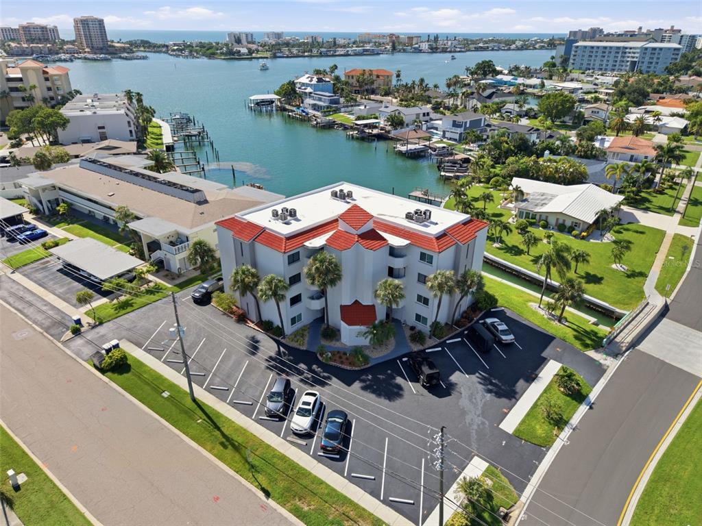 An exterior view of a multi-story apartment building with palm trees and a parking lot — 298 SKIFF POINT UNIT 103, CLEARWATER, FL