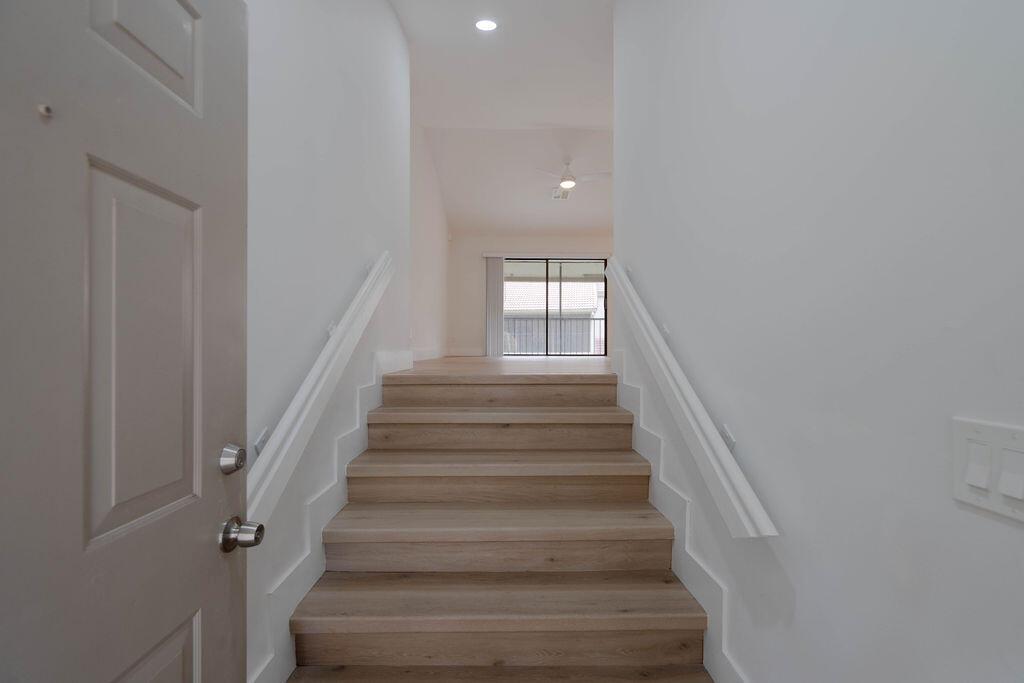 A view from an open door looking up wooden stairs toward a bright living area — 5710 Coach House Circle # G, Boca Raton FL 33486, BOCA RATON, FL