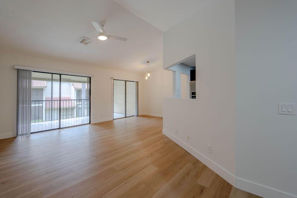 An empty living room with light wood-look flooring, a ceiling fan, and sliding glass doors — 5710 Coach House Circle # G, Boca Raton FL 33486, BOCA RATON, FL