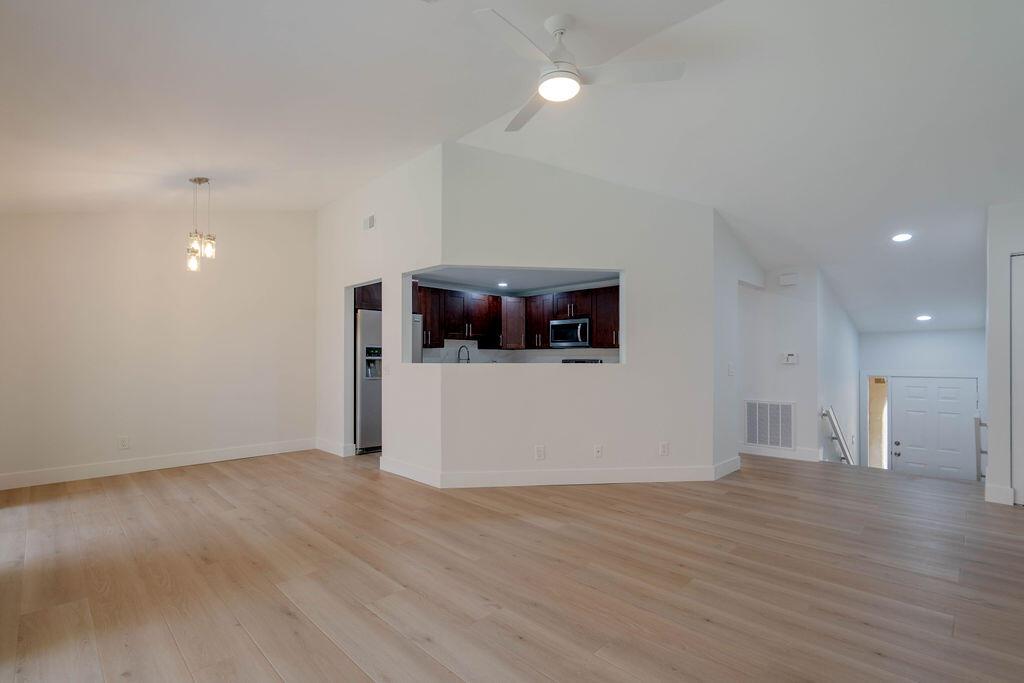 A bright, open-concept living area with light wood flooring, a ceiling fan, and kitchen pass-through — 5710 Coach House Circle # G, Boca Raton FL 33486, BOCA RATON, FL