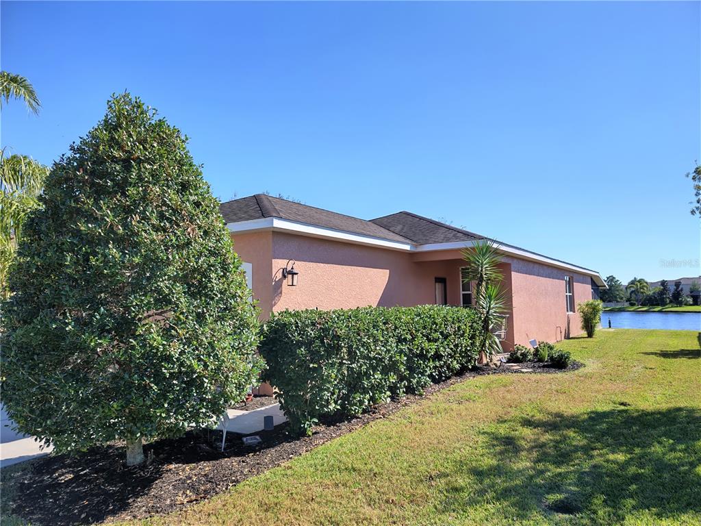 A peach-colored house exterior with a dark shingled roof, landscaping, and a nearby pond — 11997 TEMPEST HARBOR LOOP, VENICE, FL